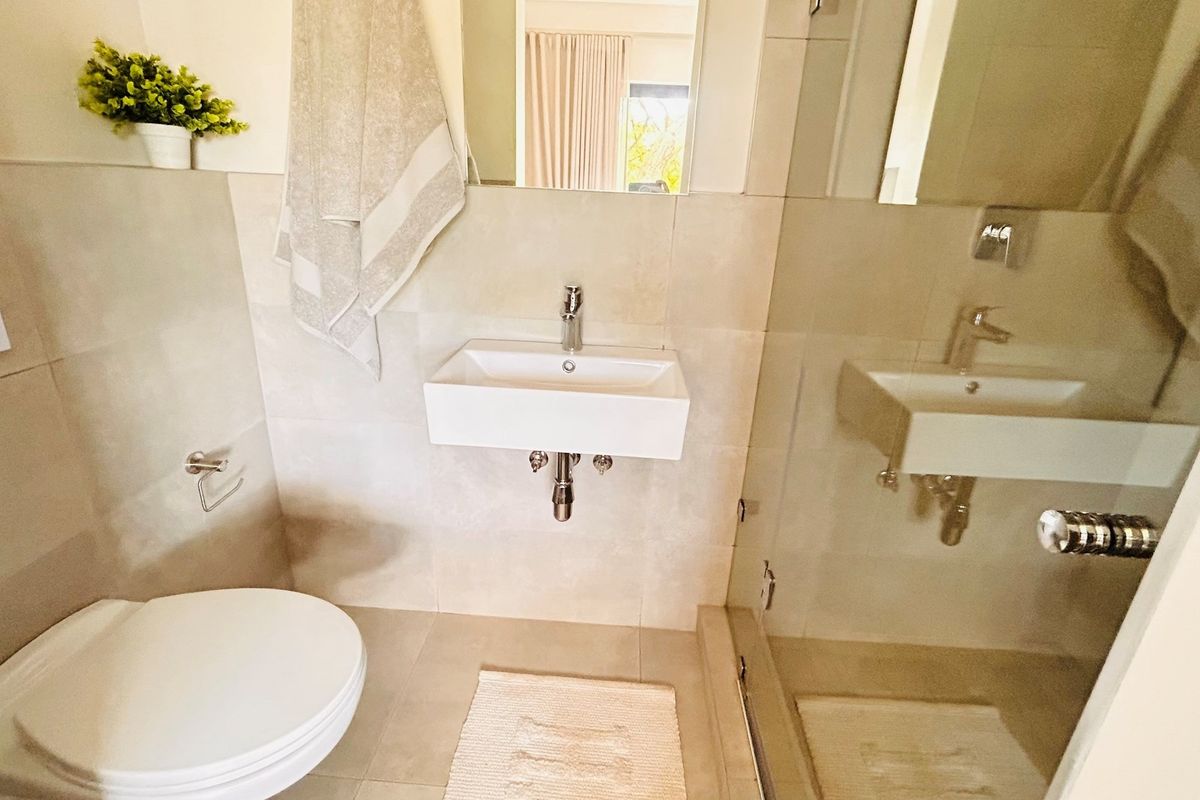 Modern bathroom featuring a wall-mounted basin, glass-enclosed shower, and neutral floor-to-ceiling tiling.
