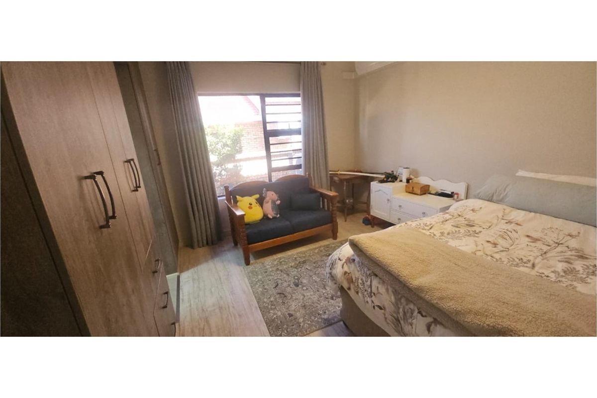 A well-lit bedroom featuring built-in wooden cabinetry, large windows with curtains, and neutral flooring.