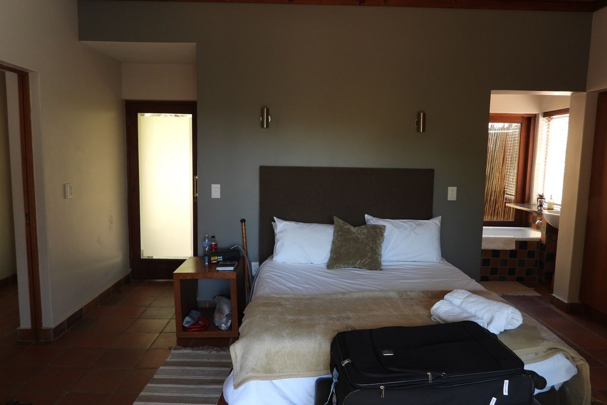 A bedroom featuring terracotta floor tiles, wall-mounted bedside lighting, and an open-plan layout leading to an en-suite bathroom area.