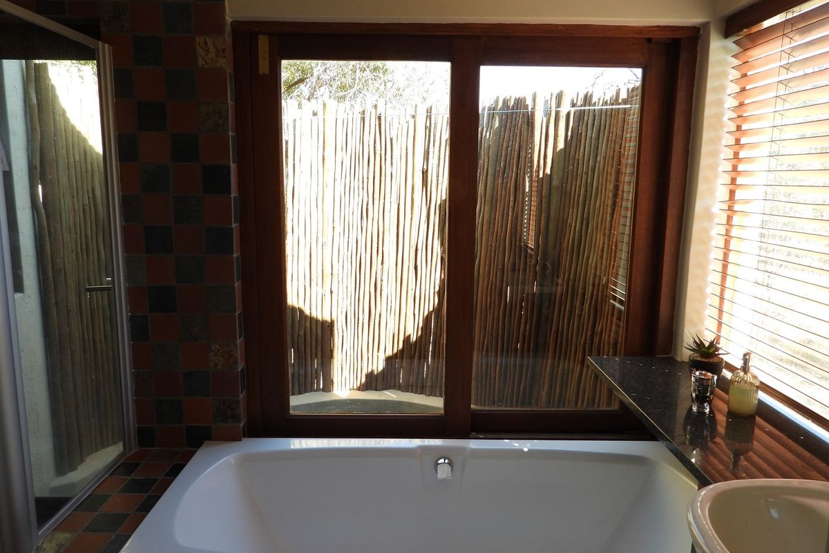 Bathroom featuring a built-in bathtub, dark granite vanity top, and sliding glass doors opening to a private outdoor area with wooden screening.