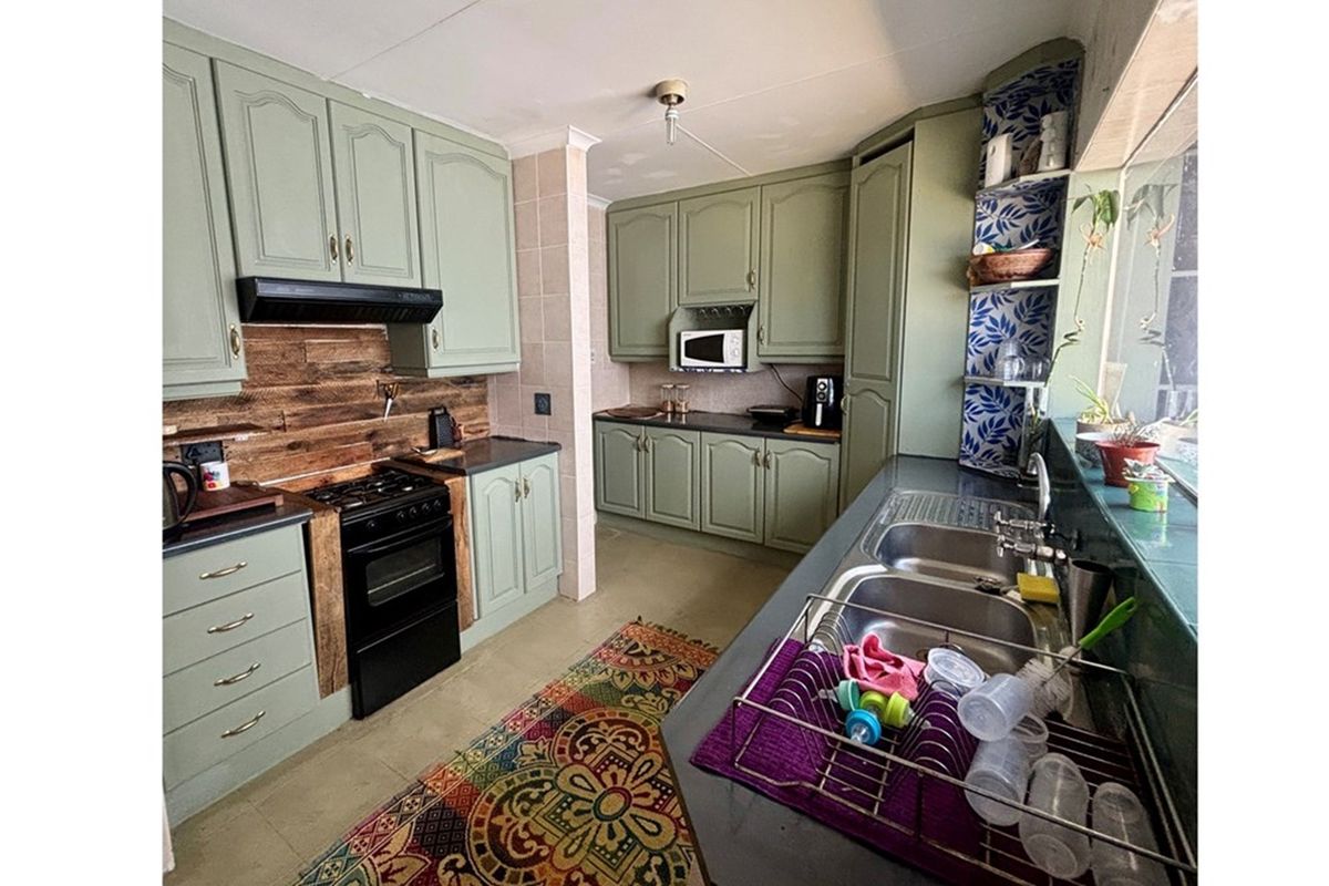 A functional kitchen featuring sage green cabinetry, dark countertops, a built-in oven with extractor fan, and a double stainless steel sink.