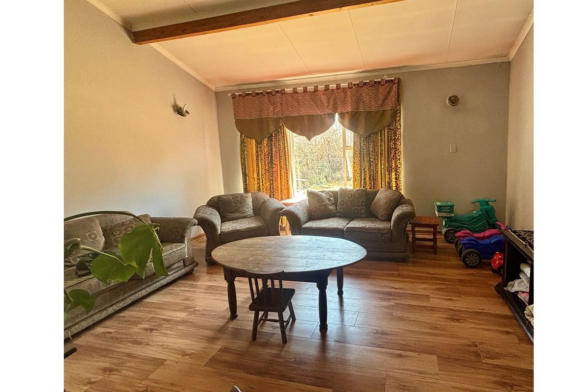 A spacious living room featuring wood-look laminate flooring, a vaulted ceiling with exposed timber beam, and large window providing natural light.