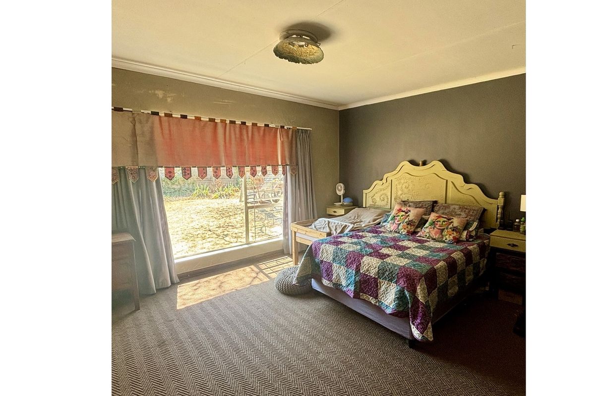 A bedroom featuring large windows with natural light, carpeted flooring, and a neutral wall finish, offering a functional space for rest.