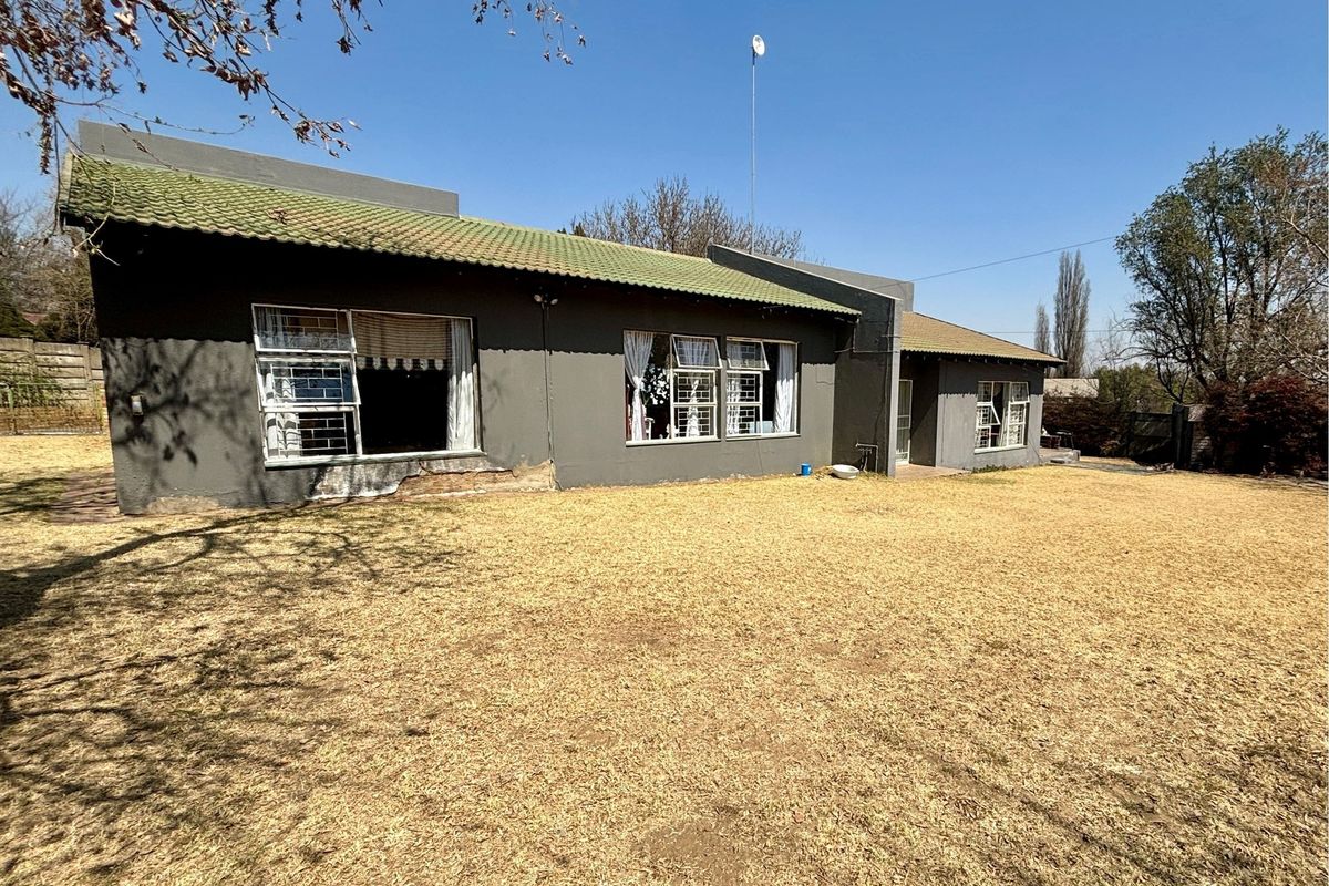 Rear view of the house featuring a dark painted exterior, tiled roof, and large windows overlooking a spacious backyard lawn.