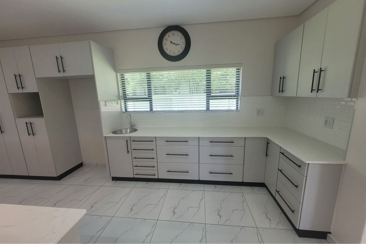 Modern kitchen featuring light grey cabinetry, white stone countertops, subway tile backsplash, and marble-look floor tiles.