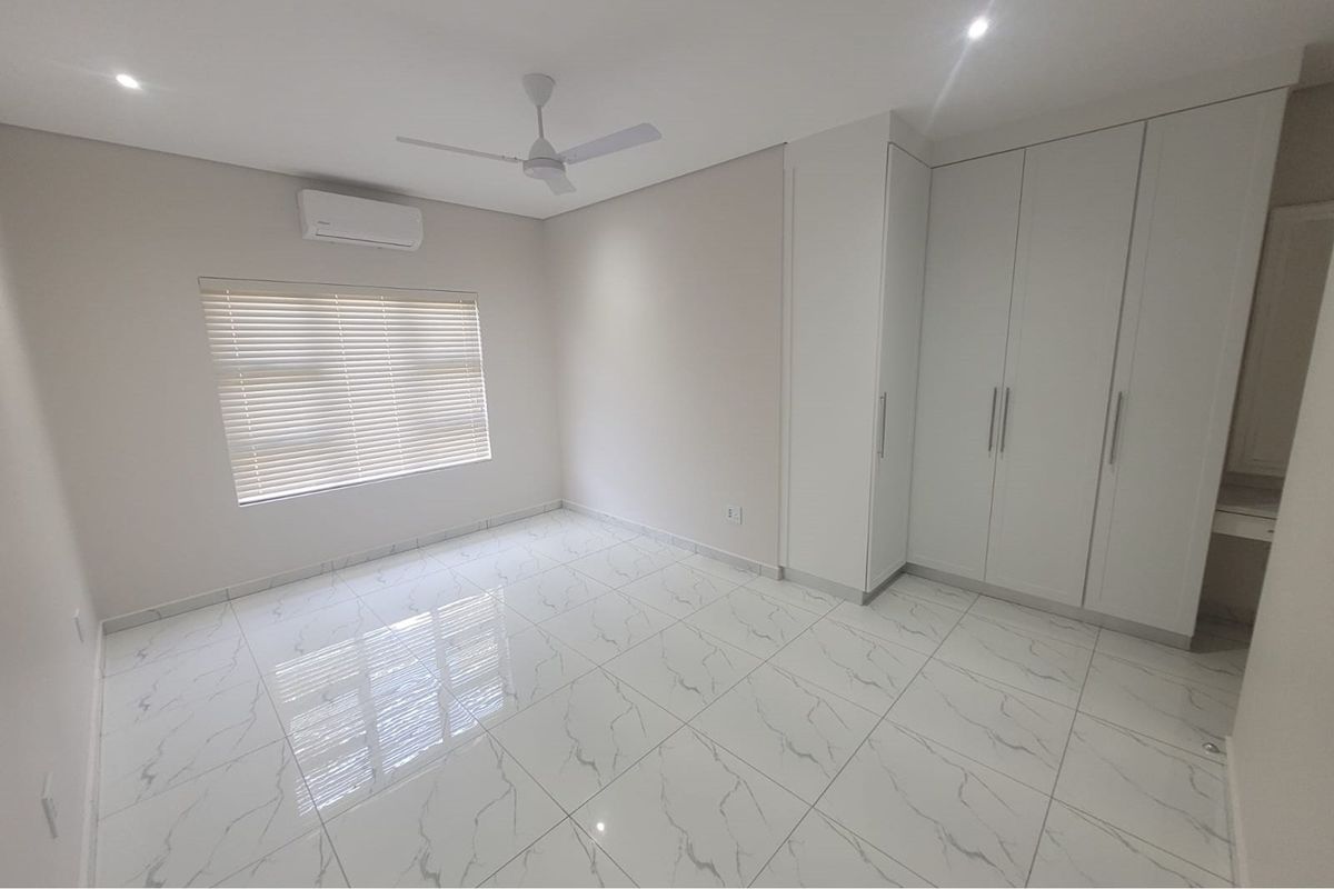 A bright, modern bedroom featuring polished marble-look floor tiles, built-in floor-to-ceiling wardrobes, a ceiling fan, and a wall-mounted air conditioning unit.