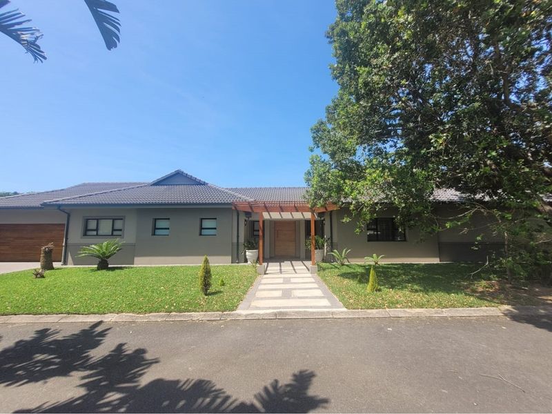 A well-maintained single-story house featuring a tiled roof, paved walkway, wooden pergola entrance, and an integrated garage.