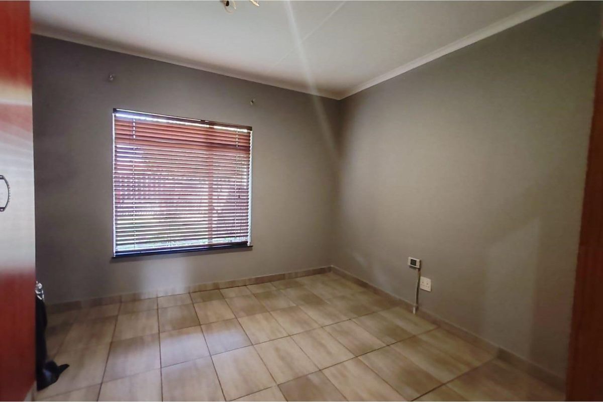 A clean, empty bedroom featuring neutral grey walls, tiled flooring, and a window fitted with wooden venetian blinds.