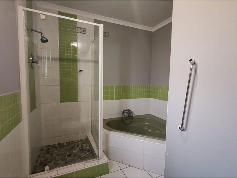 Bathroom featuring a corner bathtub, a separate glass-enclosed shower, and green accent tiling.
