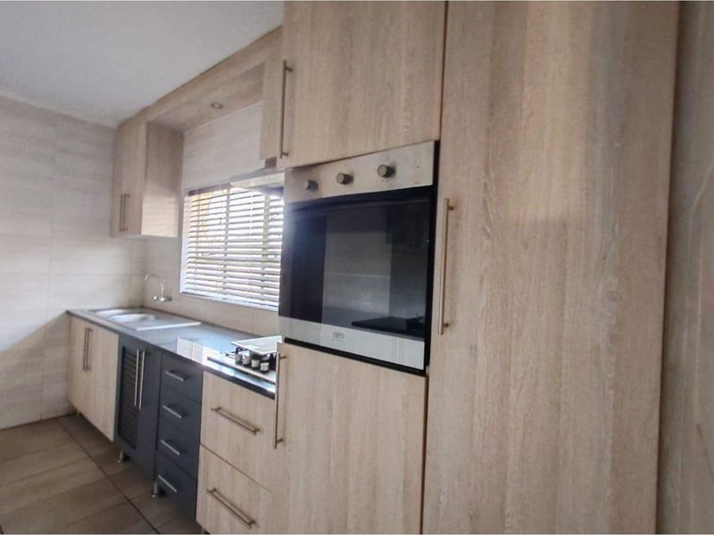 Modern kitchen featuring light wood-grain cabinetry, integrated oven, built-in hob, and a double sink with tiled flooring.