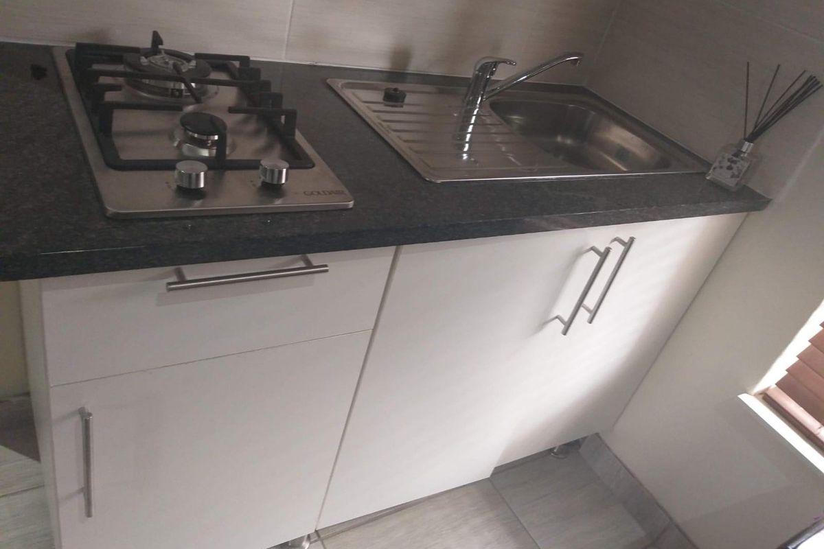 Compact kitchen area featuring a built-in gas hob, stainless steel sink, and modern white cabinetry with dark stone-look countertops.