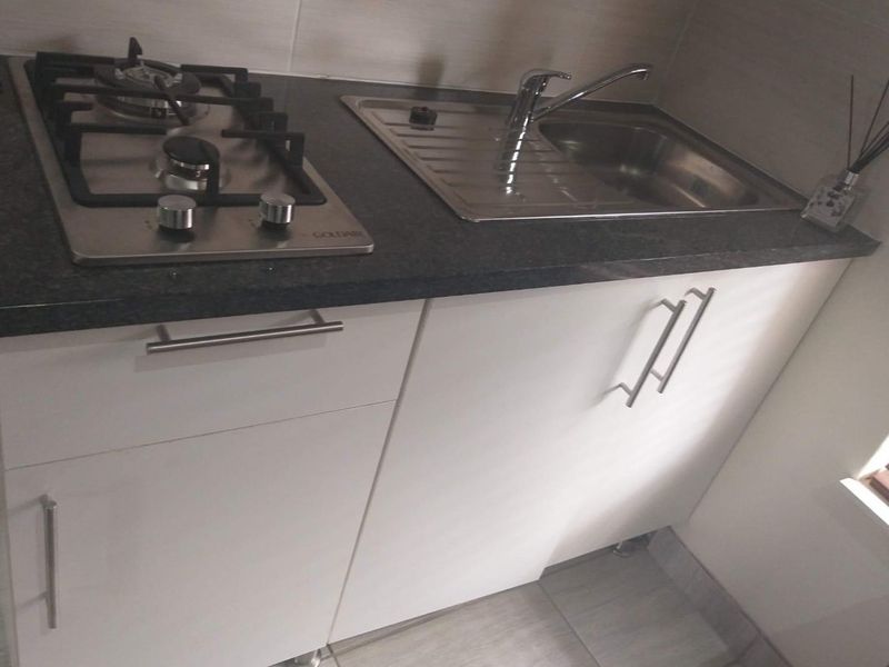 Compact kitchen area featuring a built-in gas hob, stainless steel sink, and modern white cabinetry with dark stone-look countertops.