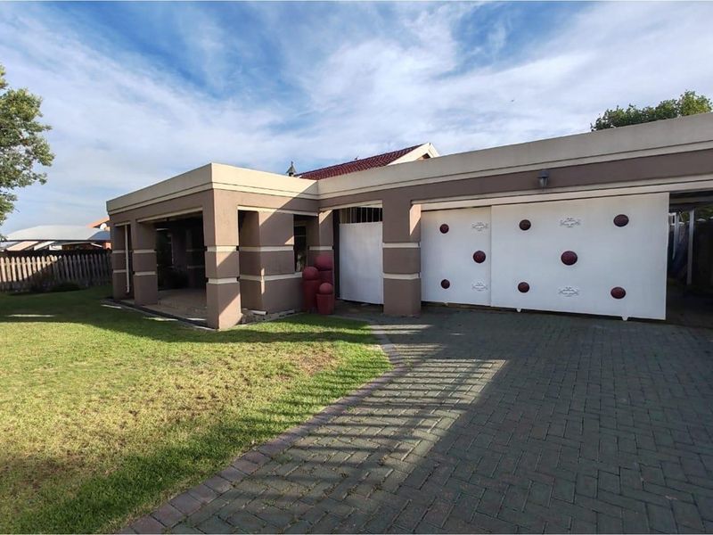 Front exterior view of the house featuring a paved driveway, double garage with decorative doors, and a covered patio area adjacent to the lawn.