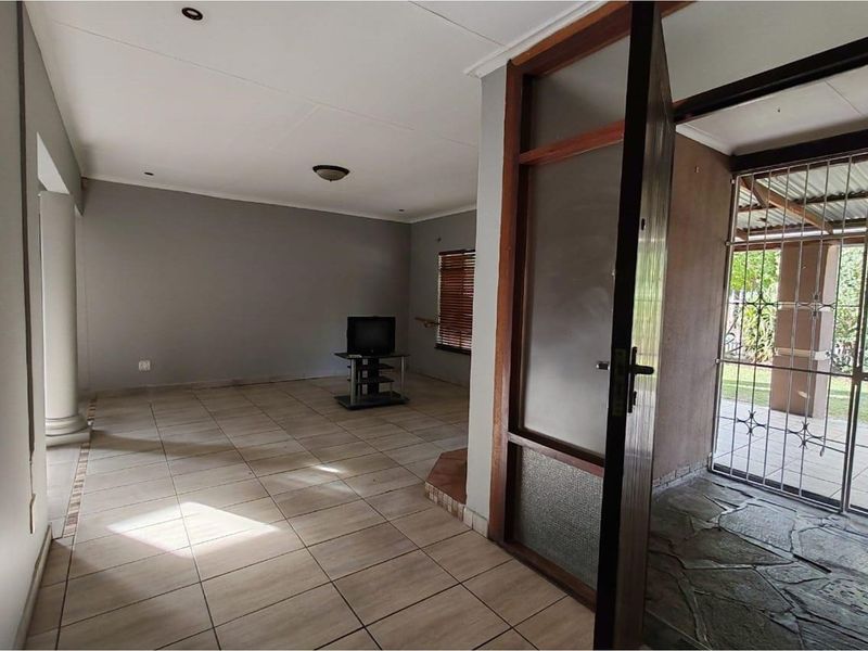 A spacious living area featuring neutral tiled flooring, recessed lighting, and a direct transition to an enclosed patio space through a wooden door.