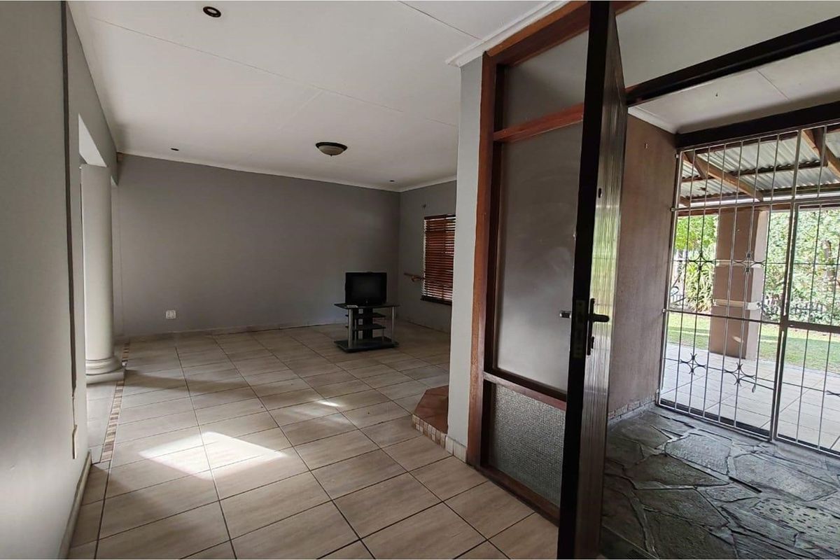 A spacious living area featuring neutral tiled flooring, recessed lighting, and a direct transition to an enclosed patio space through a wooden door.