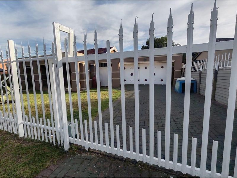 Front view of the property featuring a paved driveway, double garage, and secure white metal perimeter fencing.
