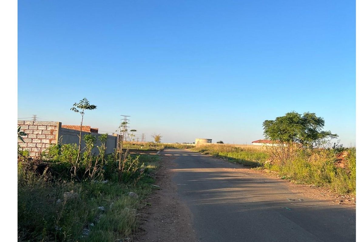 A view of the asphalt access road leading to the vacant residential land, featuring surrounding boundary walls and open landscape.