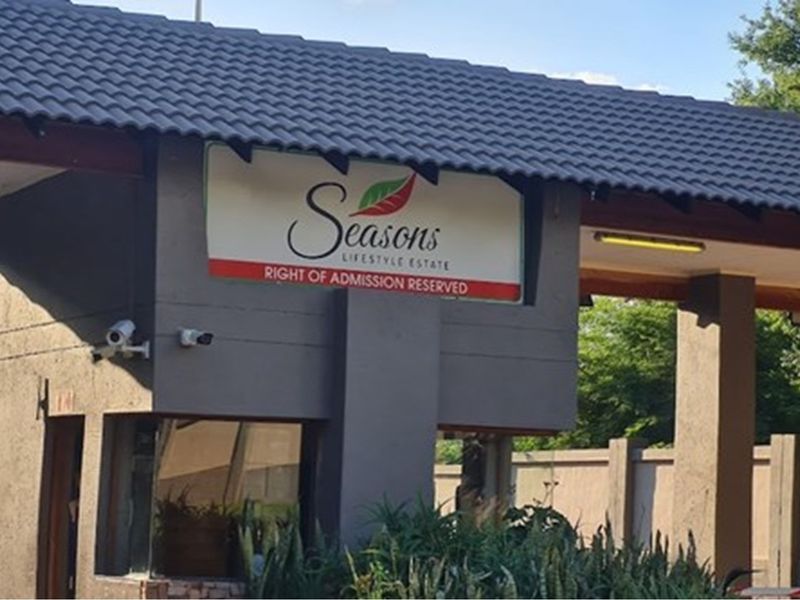 Entrance gate and security checkpoint for Seasons Lifestyle Estate, featuring a tiled roof structure and estate signage.