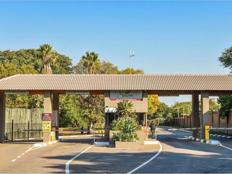 A well-maintained residential estate entrance featuring a security gatehouse, boom gates, and paved access roads.