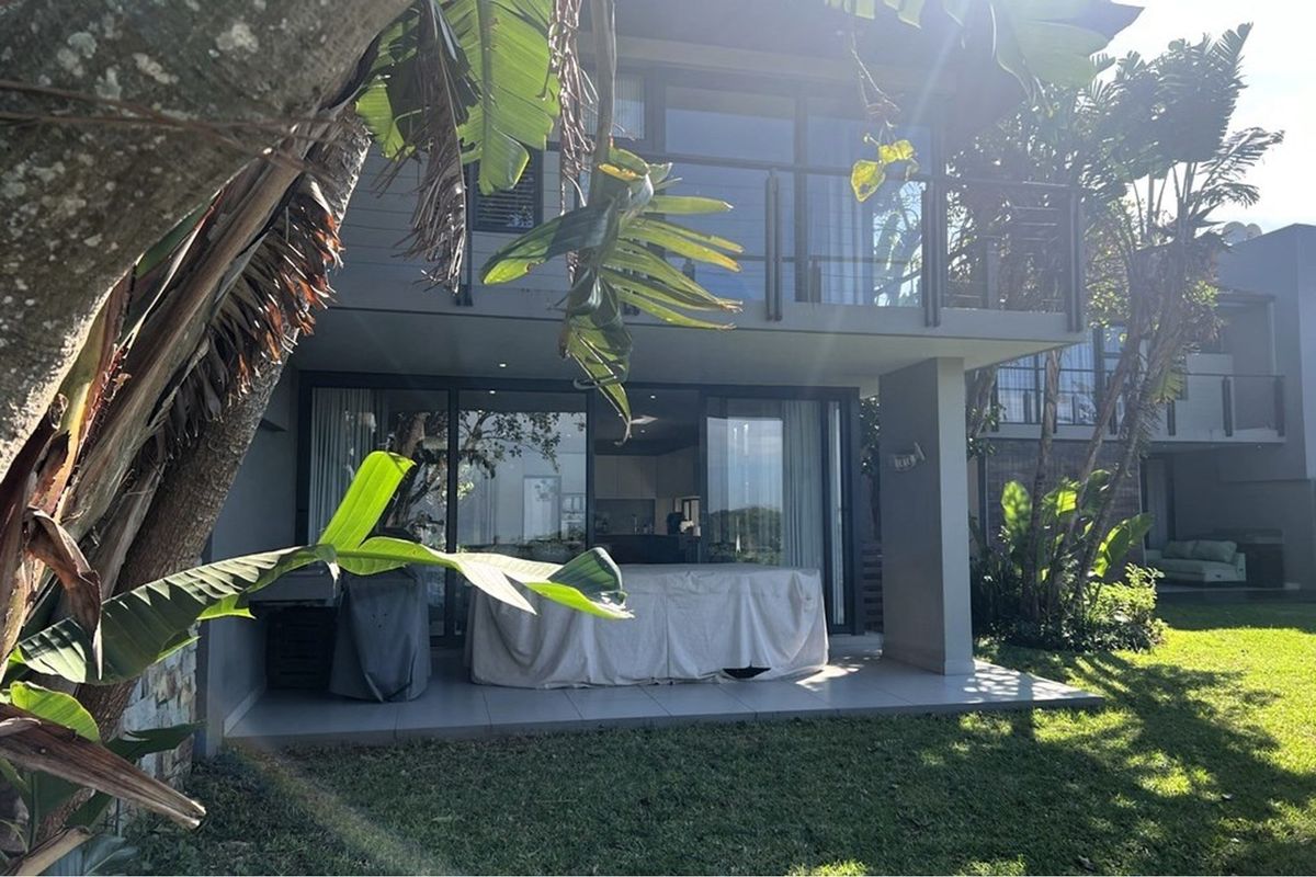A rear view of the property featuring a covered patio with tiled flooring, large sliding glass doors, and an upper-level balcony.
