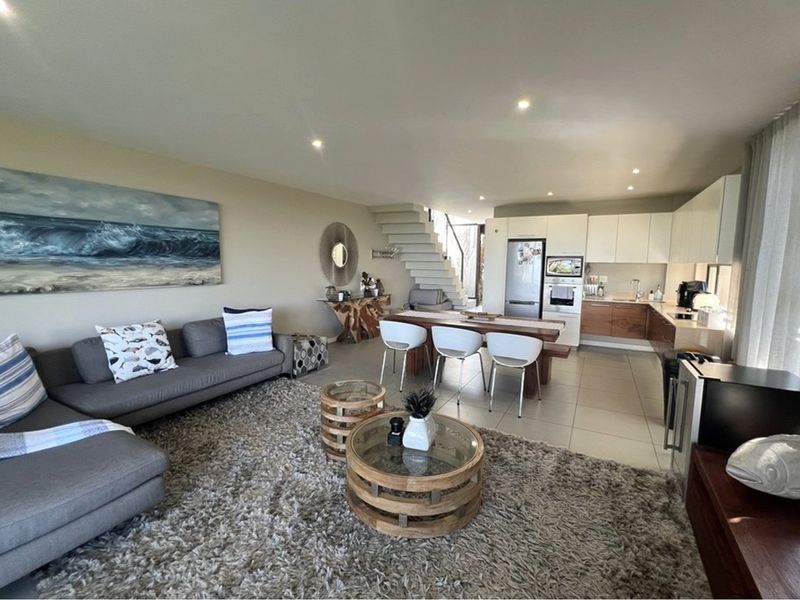Spacious open-plan living area featuring a modern kitchen with built-in cabinetry, integrated appliances, tiled flooring, and a staircase leading to the upper level.