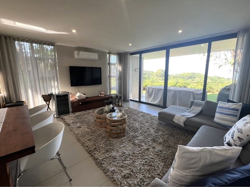 A bright open-plan living and dining area featuring large format floor tiles, recessed lighting, and expansive sliding glass doors leading to an outdoor space.