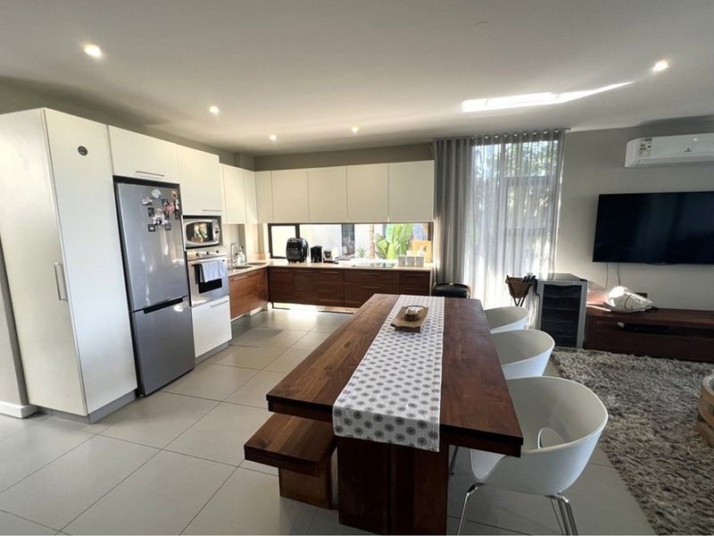 Modern open-plan living area featuring a contemporary kitchen with two-tone cabinetry, integrated appliances, and seamless flow to the dining and lounge space.