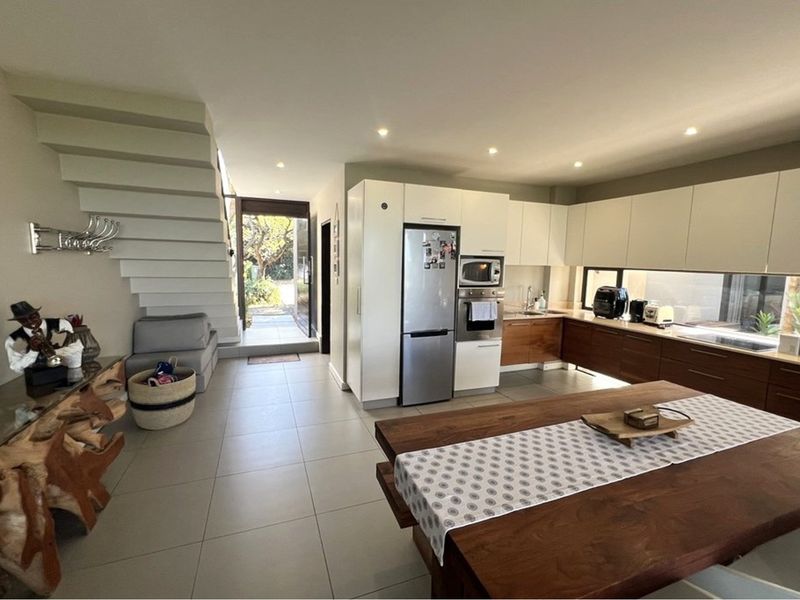 Modern open-plan kitchen featuring sleek cabinetry, integrated appliances, and tiled flooring, seamlessly connected to the living area and staircase.