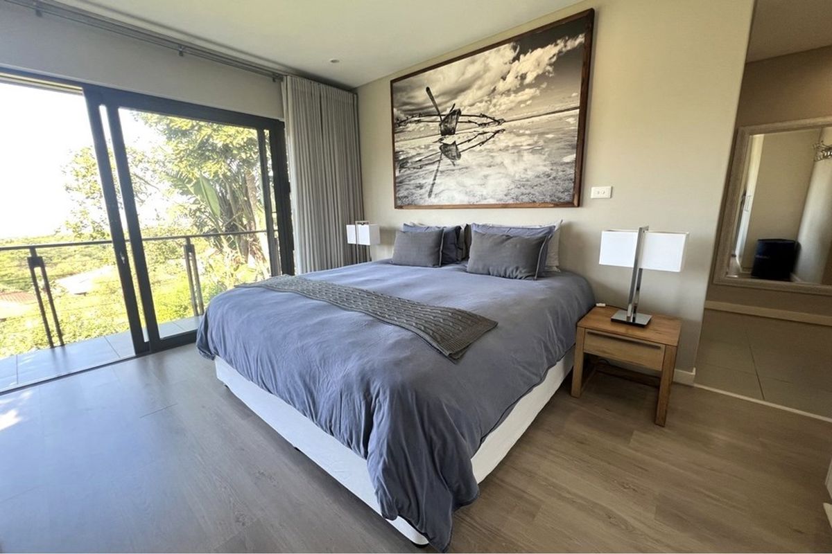 A well-maintained bedroom featuring modern laminate flooring, recessed lighting, and large sliding glass doors opening onto a private balcony.