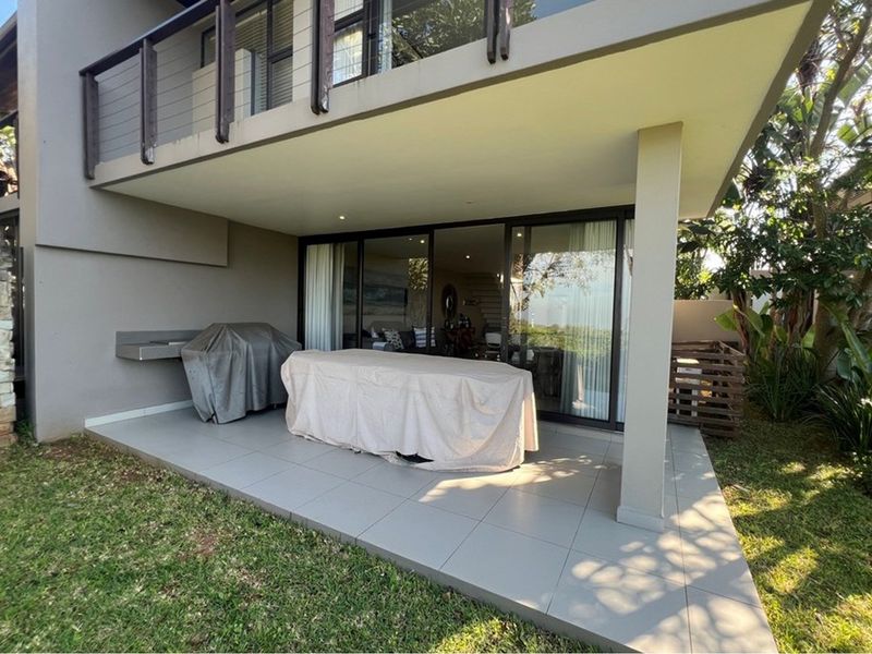 Covered ground-floor patio featuring tiled flooring, a built-in braai, and direct access to the living area through large sliding glass doors.