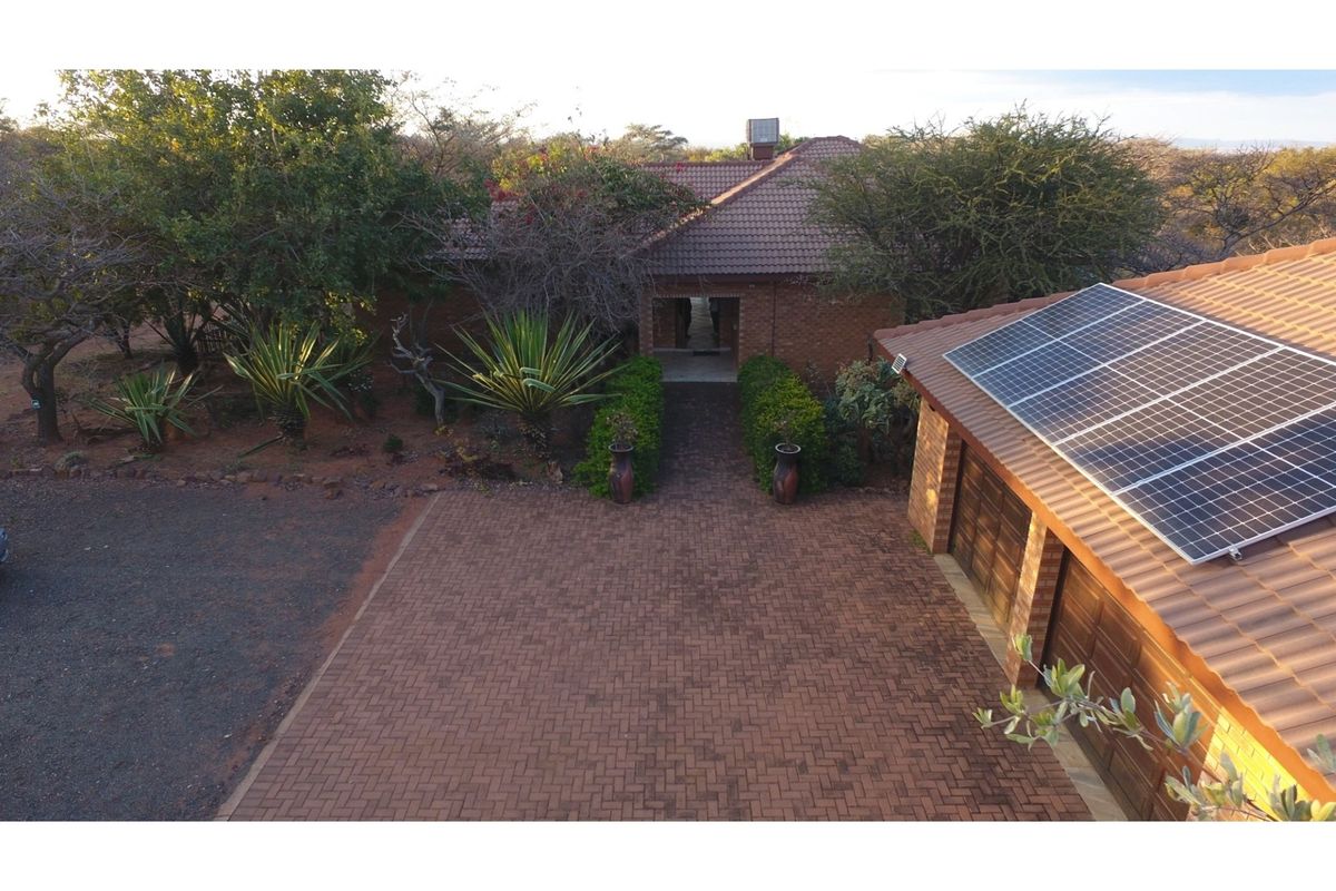 Aerial view of the property entrance featuring a paved driveway, double garage with solar panels, and established garden landscaping.