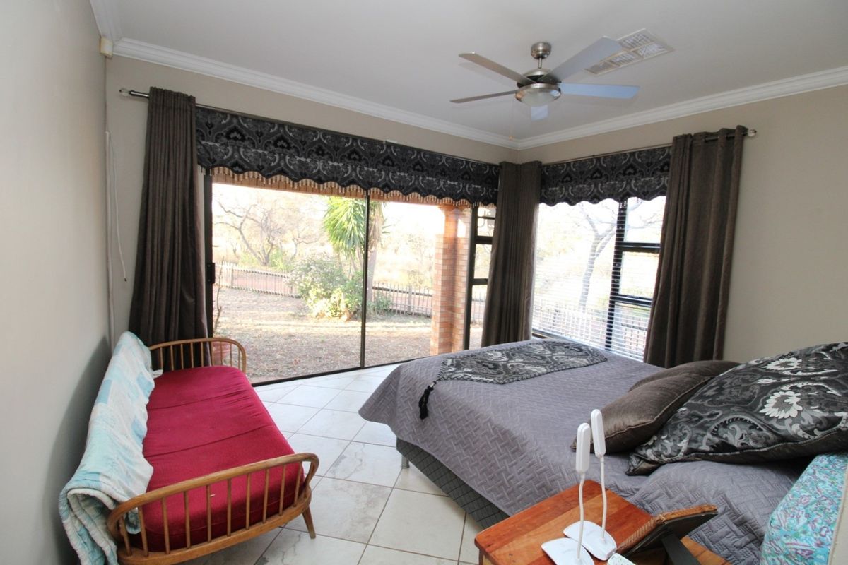 A spacious bedroom featuring large sliding glass doors that open to the garden, tiled flooring, and a ceiling fan.