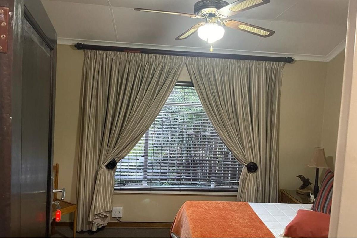 A bedroom featuring a ceiling fan, window with blinds, and curtain rods.