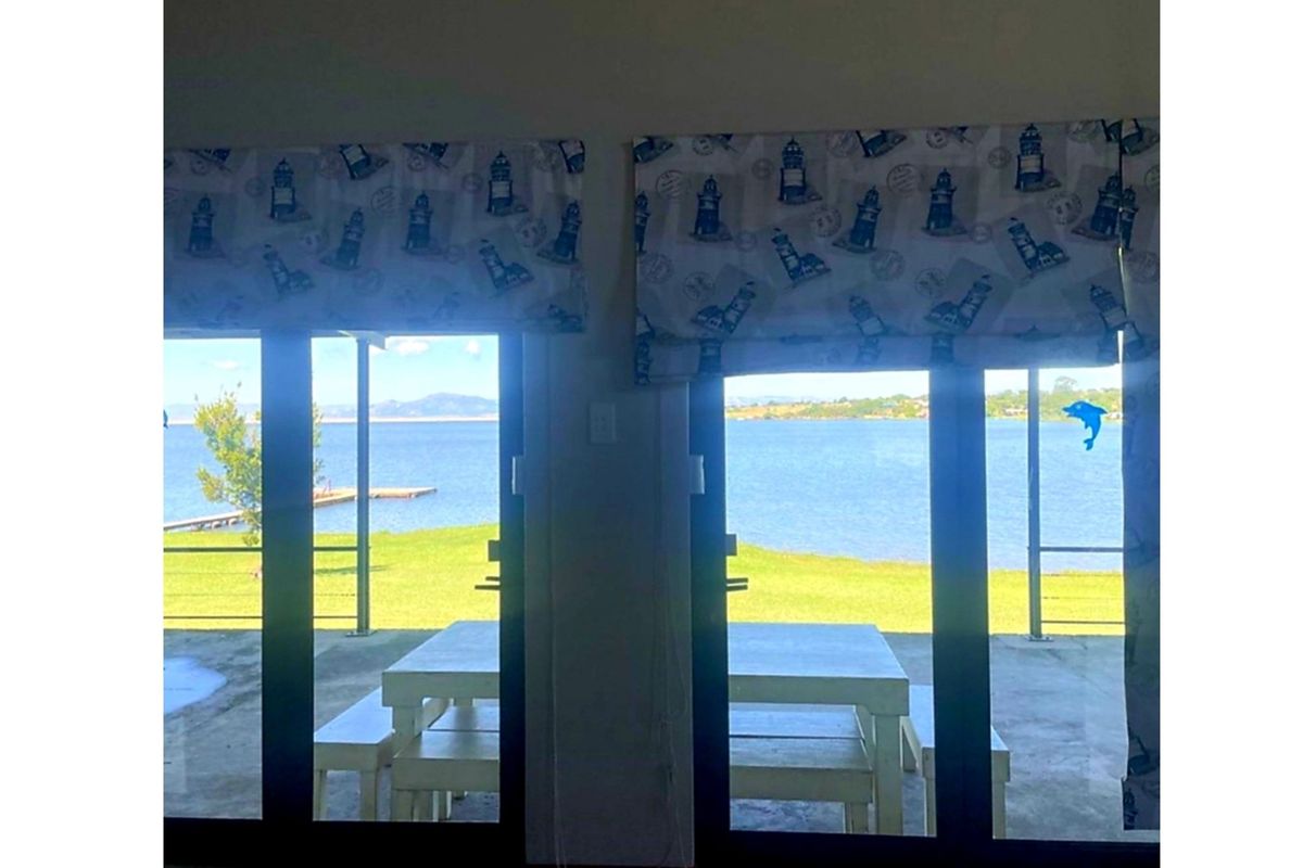 A view from the interior looking out through sliding glass doors towards a waterfront garden and jetty.