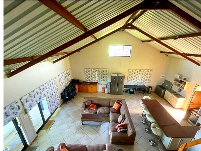 Spacious open-plan living area featuring high-pitched ceilings with exposed steel trusses, tiled flooring, and an integrated kitchen layout with ample cabinetry.