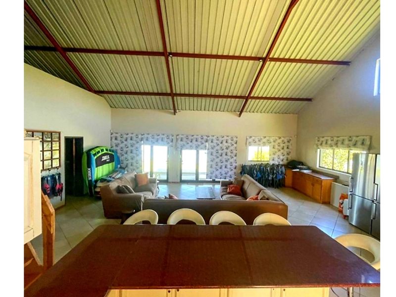 Spacious open-plan living area featuring high vaulted ceilings with exposed steel trusses, tiled flooring, and direct access to the outdoors through sliding glass doors.