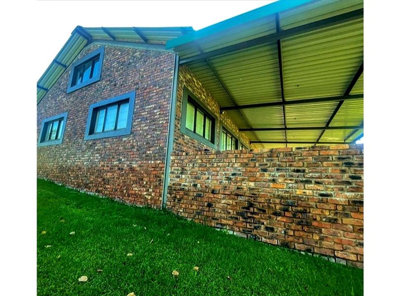 A rear view of the house featuring a face brick exterior, aluminium window frames, and a spacious covered patio area.