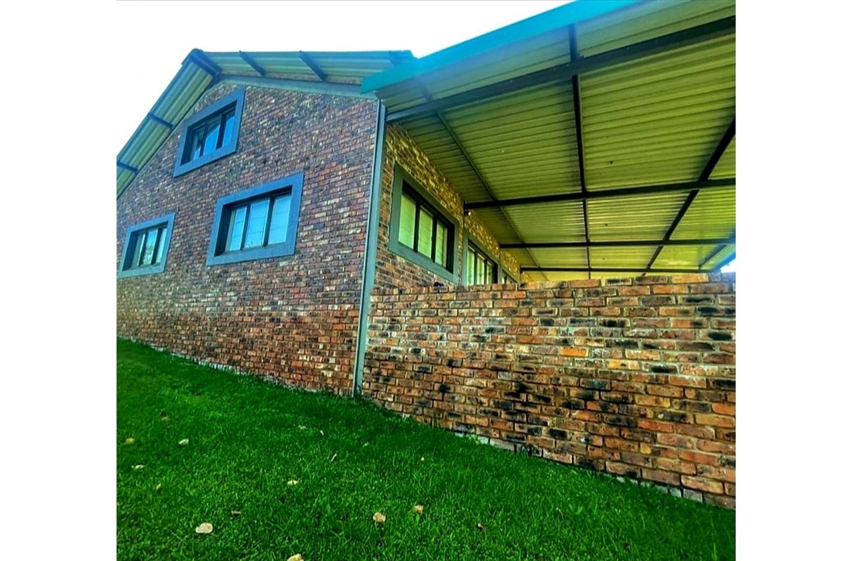 A rear view of the house featuring a face brick exterior, aluminium window frames, and a spacious covered patio area.