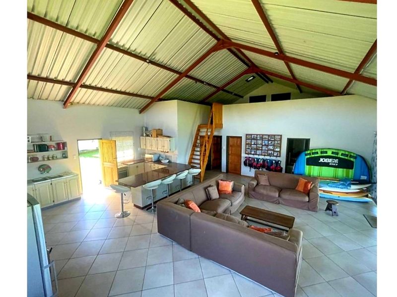 Spacious open-plan living area featuring a kitchen with island, tiled floors, and a high pitched ceiling with exposed steel trusses and a mezzanine level.
