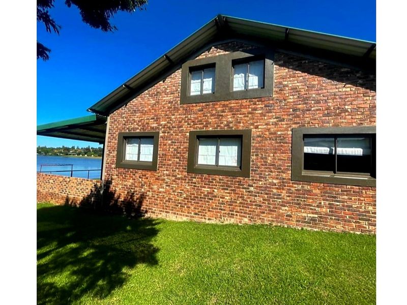 A view of the rear face brick exterior of the house, featuring a metal roof and a brick boundary wall overlooking the water.