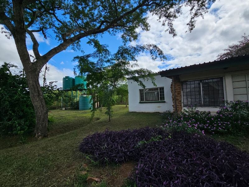 Rear view of the property featuring a garden, established trees, and external water storage tanks.