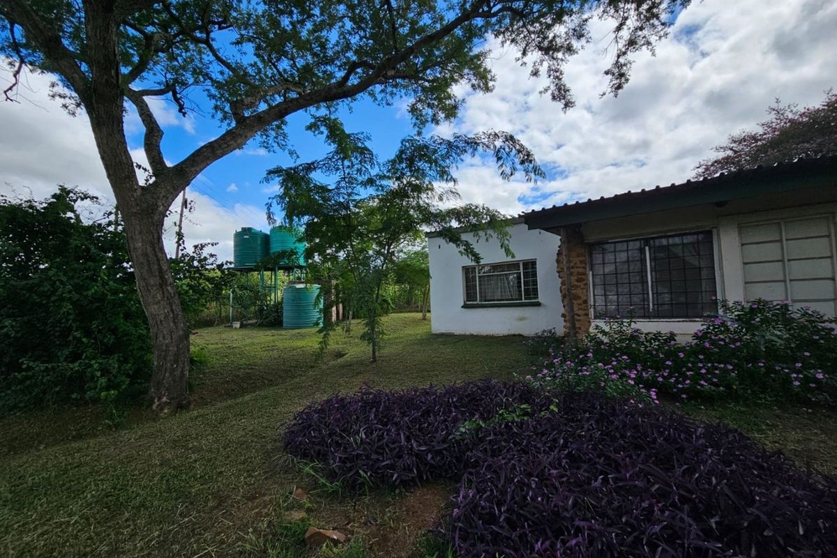 Rear view of the property featuring a garden, established trees, and external water storage tanks.