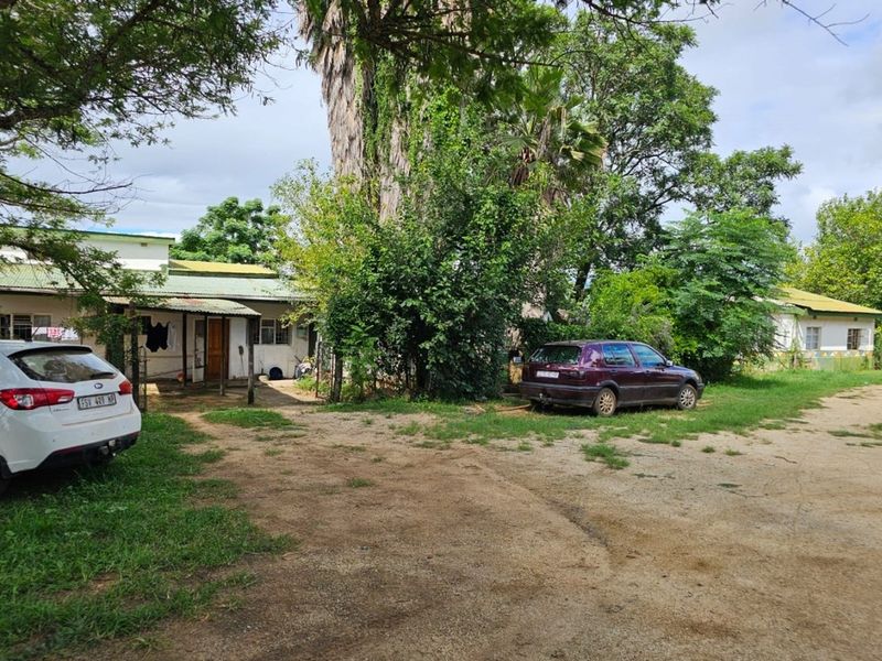 Front view of a small holding property featuring a single-story dwelling with a covered porch and an expansive unpaved driveway area.