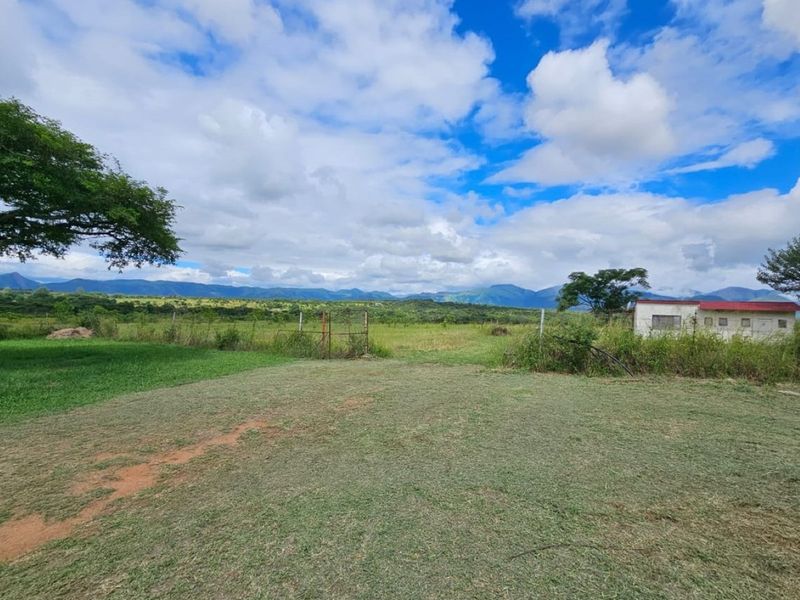 Expansive rural landscape view featuring open grassland, mountain backdrop, and a small outbuilding on the property grounds.