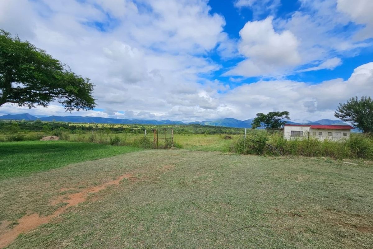Expansive rural landscape view featuring open grassland, mountain backdrop, and a small outbuilding on the property grounds.