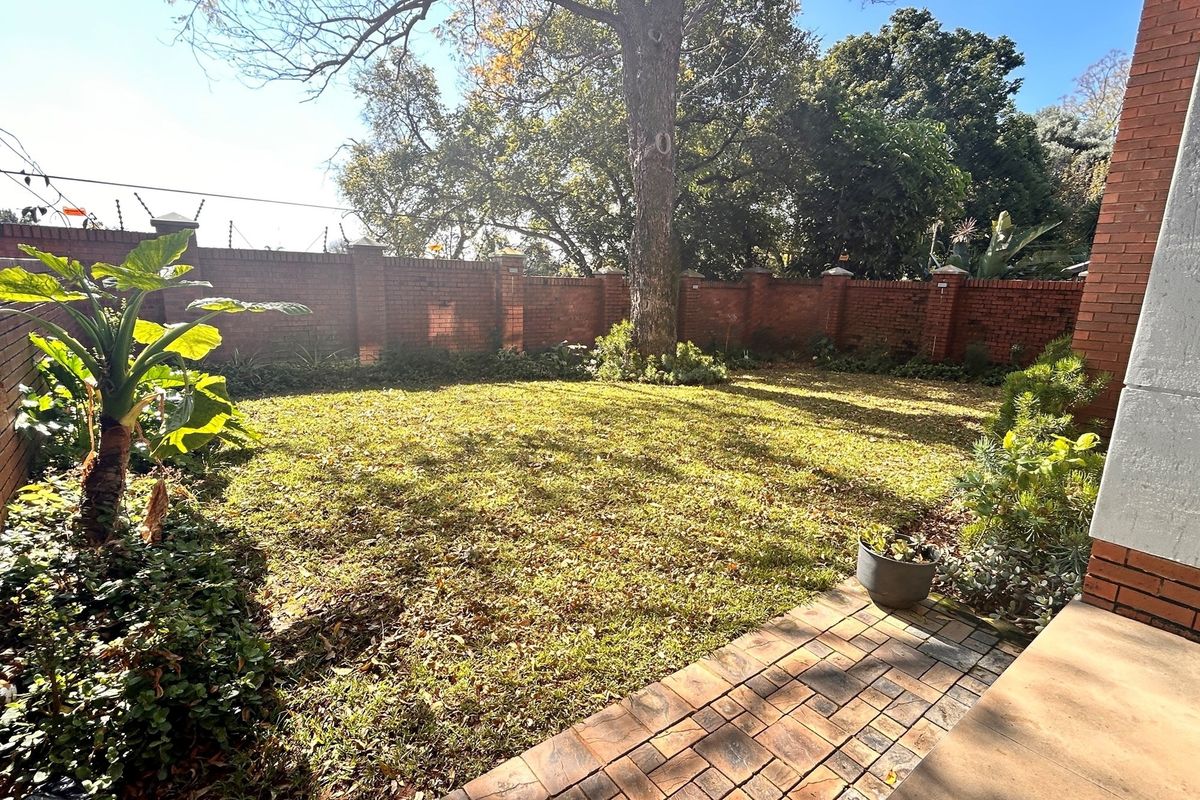 A private rear garden featuring a paved patio area, established lawn, and perimeter brick walling with security fencing.