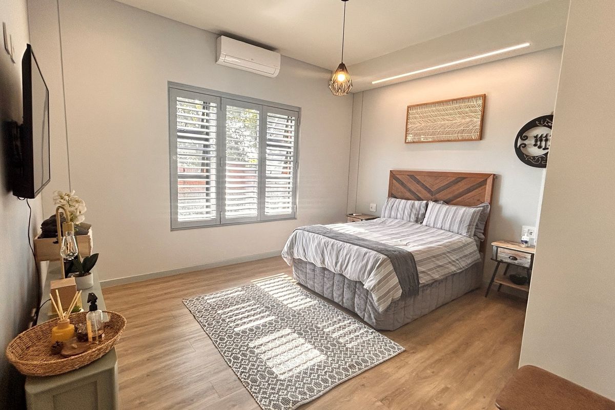 A well-maintained bedroom featuring light wood-look flooring, a wall-mounted air conditioning unit, and modern window shutters.