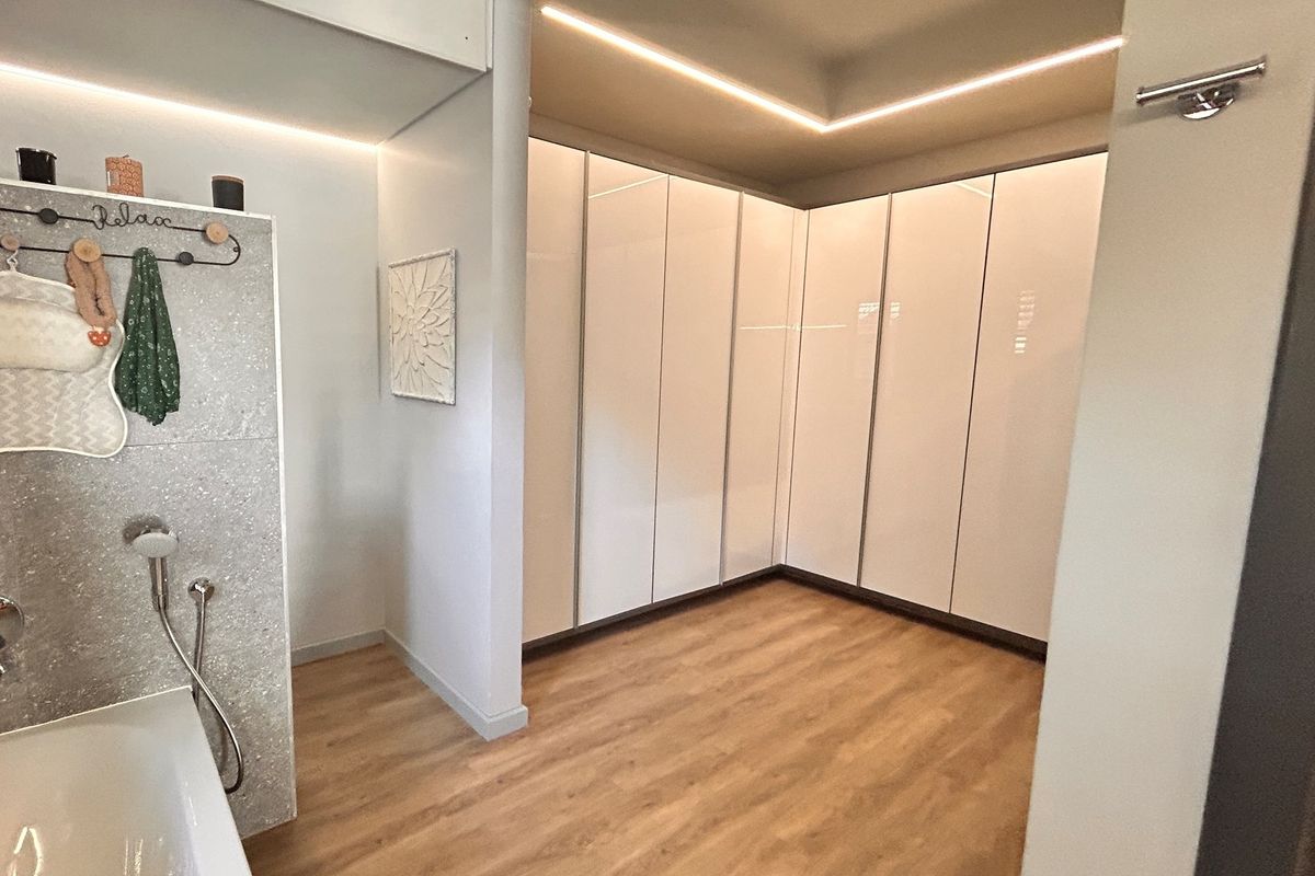 Modern bathroom featuring sleek white built-in cabinetry, integrated LED cove lighting, and high-quality wood-look flooring.