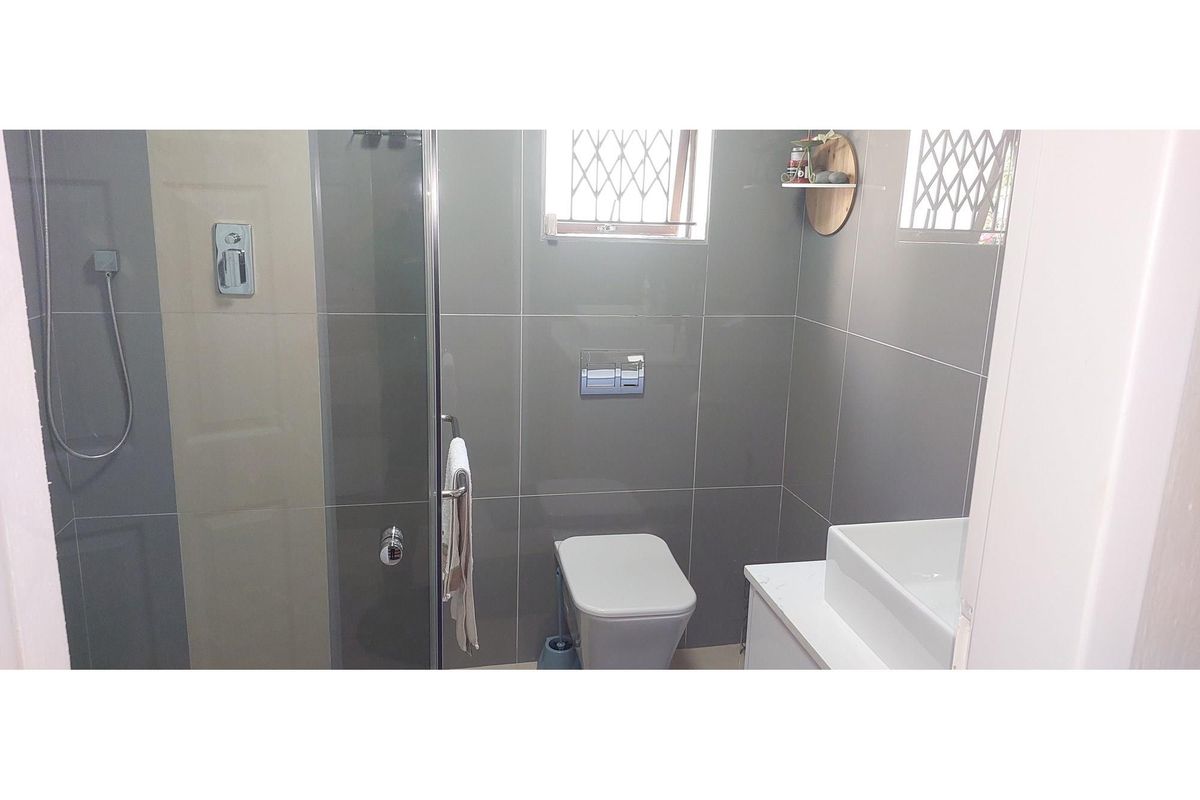 Modern bathroom featuring grey wall tiles, a glass-enclosed shower, a wall-mounted toilet, and a contemporary vanity basin.