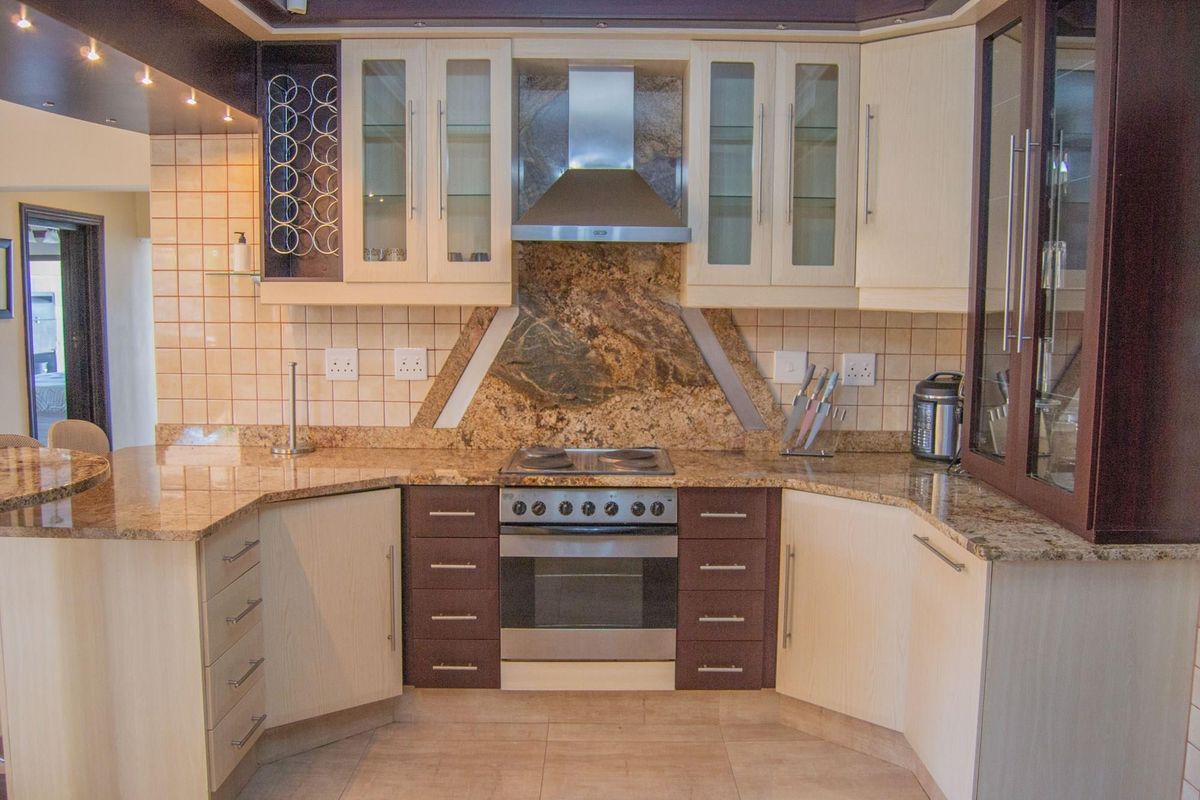 A well-appointed kitchen featuring granite countertops, built-in oven, electric hob, stainless steel extractor fan, and ample cabinetry with integrated wine storage.